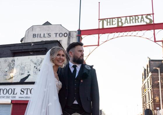 Bride and Groom stand under Barras sign in Glasgow
