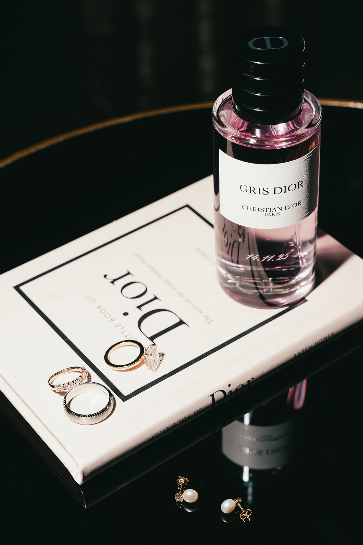 Wedding detail flatlay with Dior perfume, wedding rings and book styling for bridal morning