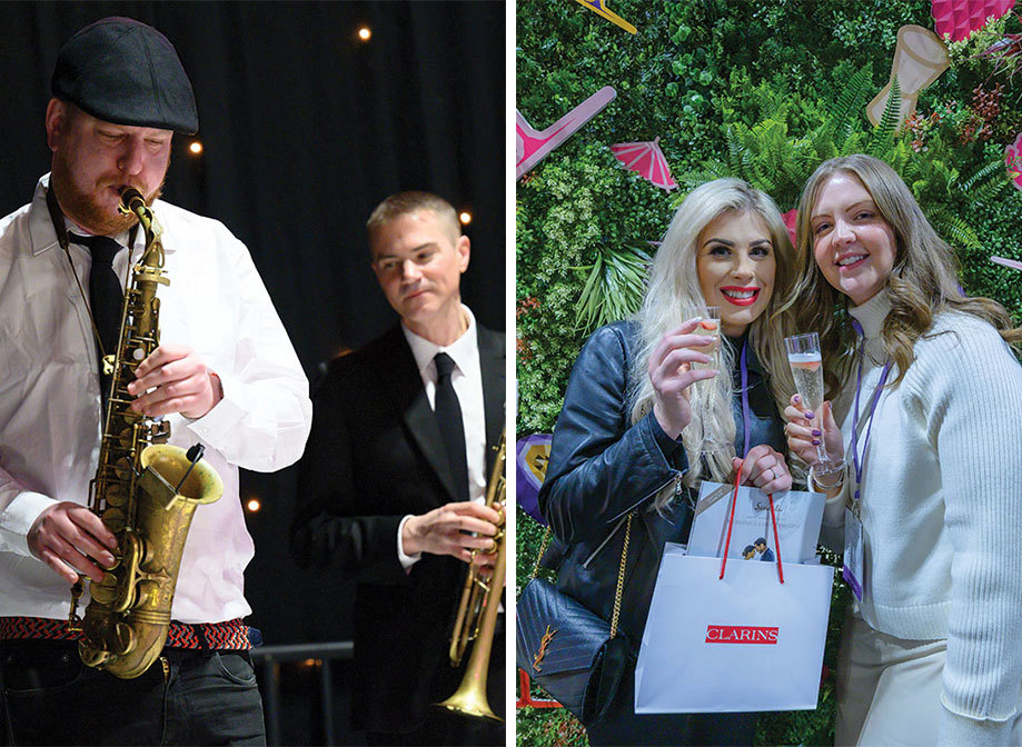 A person playing the saxophone with a person holding a trumpet behind them on left. Two people with plastic champagne flutes standing against a green wall covered in plastic foliage and colourful decals