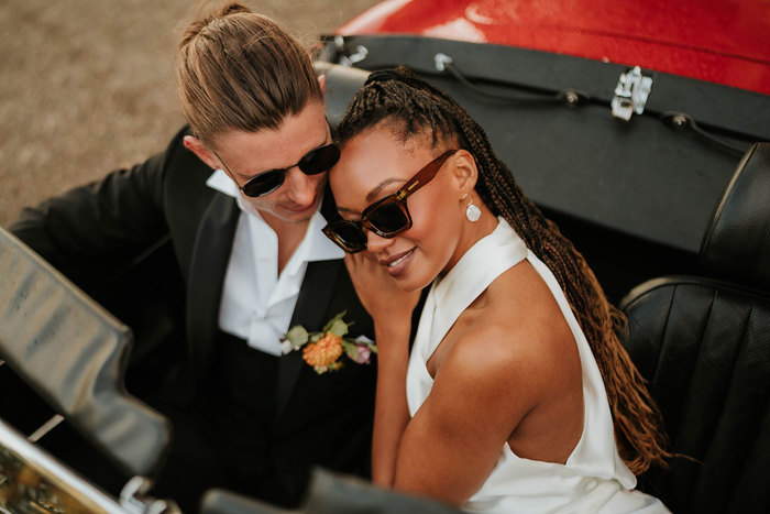 The bride and groom cosy up to one another inside convertible while sporting sunglasses