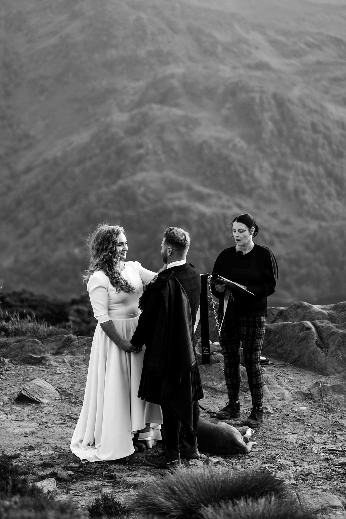 Black and white photograph of a couple exchanging vows during an outdoor Scottish elopement ceremony with their dog beside them