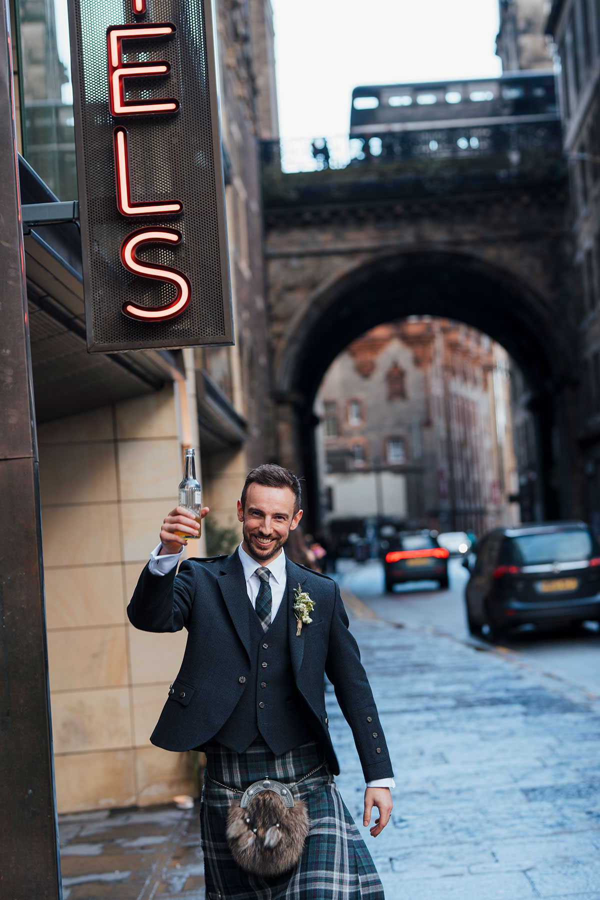 groom walks through streets of edinburgh with beer in hand during wedding at Virgin Hotels Edinburgh