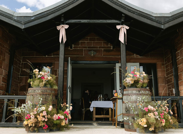 the red brick exterior of Dougarie Boathouse with black pitched roof. The doorway is flanked by two whisky barrels decorated with floral arrangements and black pillars have a red and white bow decoration