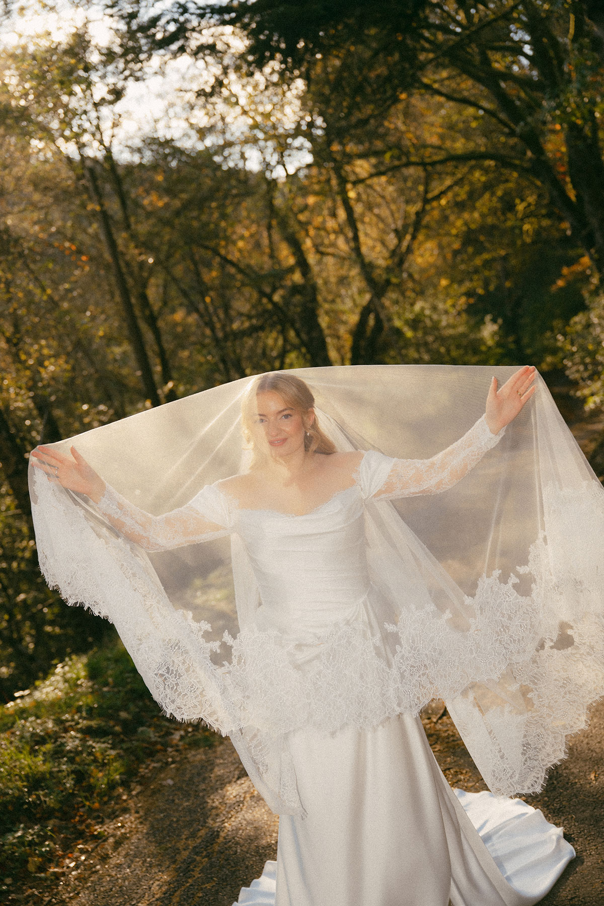 Bride holding lace veil wide in golden autumn woodland light during Scottish wedding photoshoot