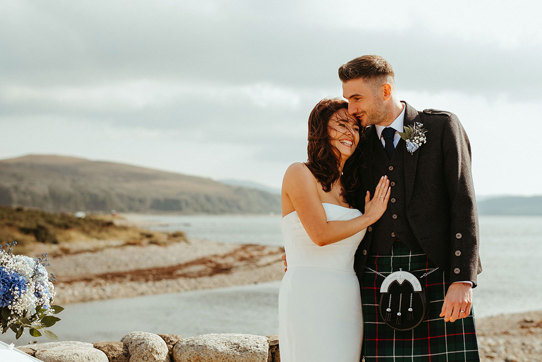 bride and groom laugh together as they stand next to stone wall during dougarie boathouse wedding