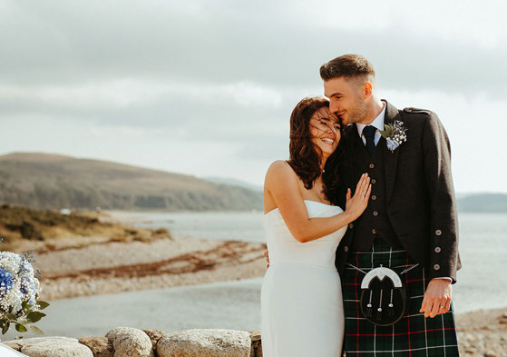 bride and groom laugh together as they stand next to stone wall during dougarie boathouse wedding