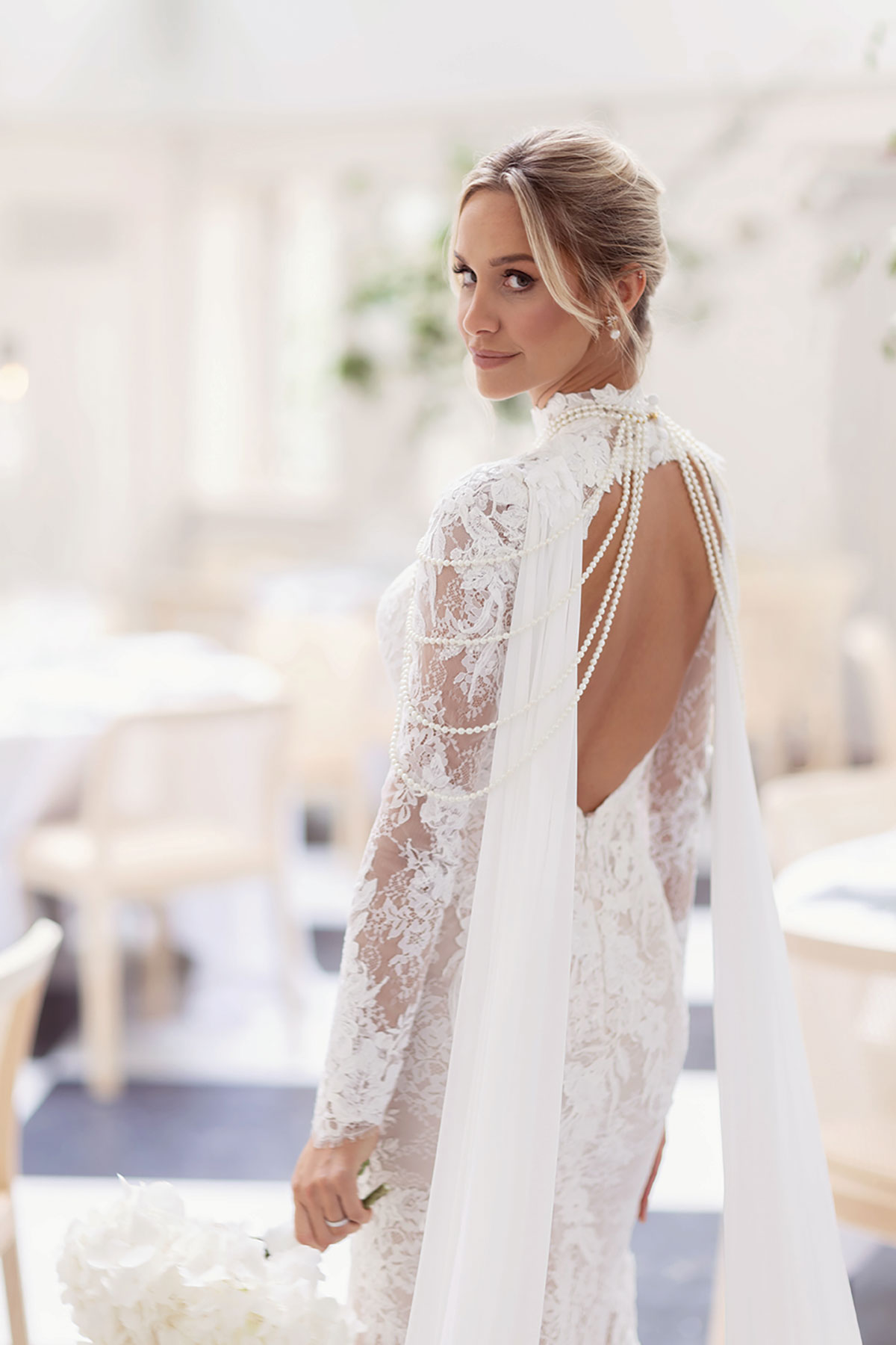 Bride with pearl-draped open back lace gown holding white bouquet