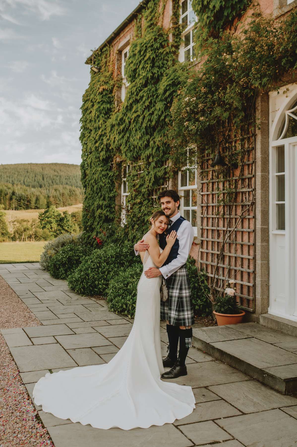 Bride and groom embrace beside the ivy-covered exterior of Ballogie House after their wedding