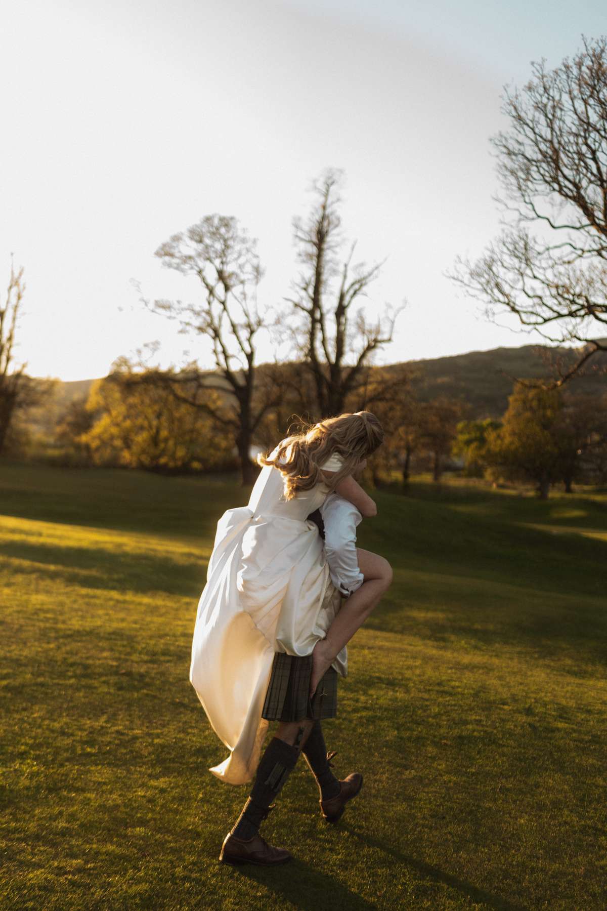 Stuart carries Siân through the grounds of Mar Hall during golden hour after their spring wedding in Renfrewshire.