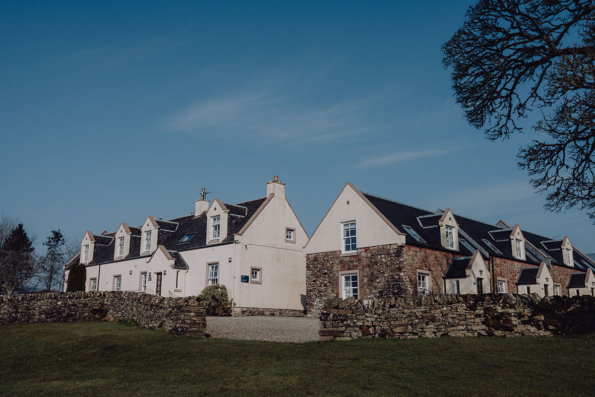 Exterior of Ardoch Loch Lomond wedding venue, with whitewashed and stone buildings surrounded by gardens and countryside.