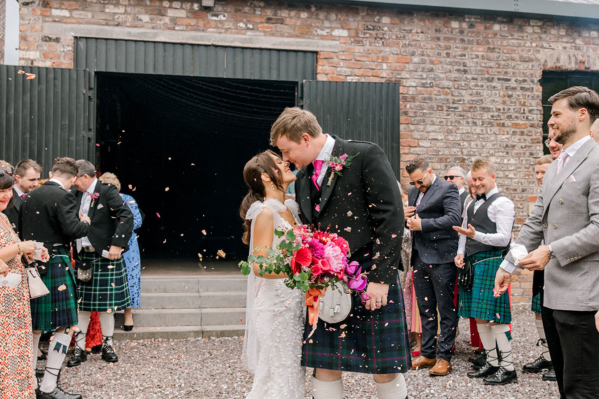 Bride and groom kissing during a confetti throw outside their industrial wedding venue