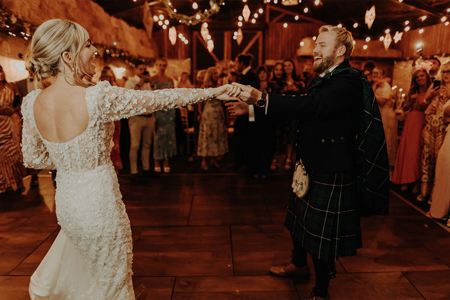 A bride and groom dancing in a barn under fairylights