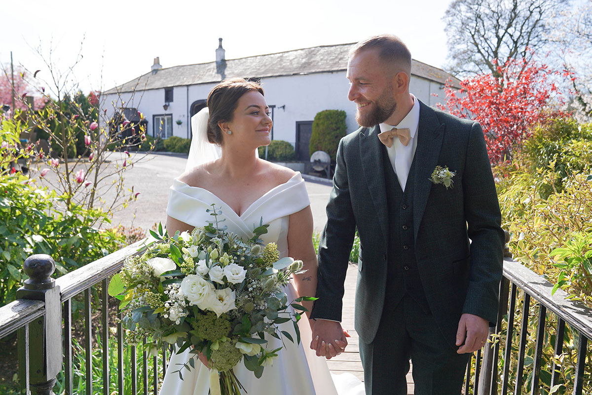 Newlyweds walking through the gardens at Gretna Hall, one of Gretna Green's historic wedding venues.