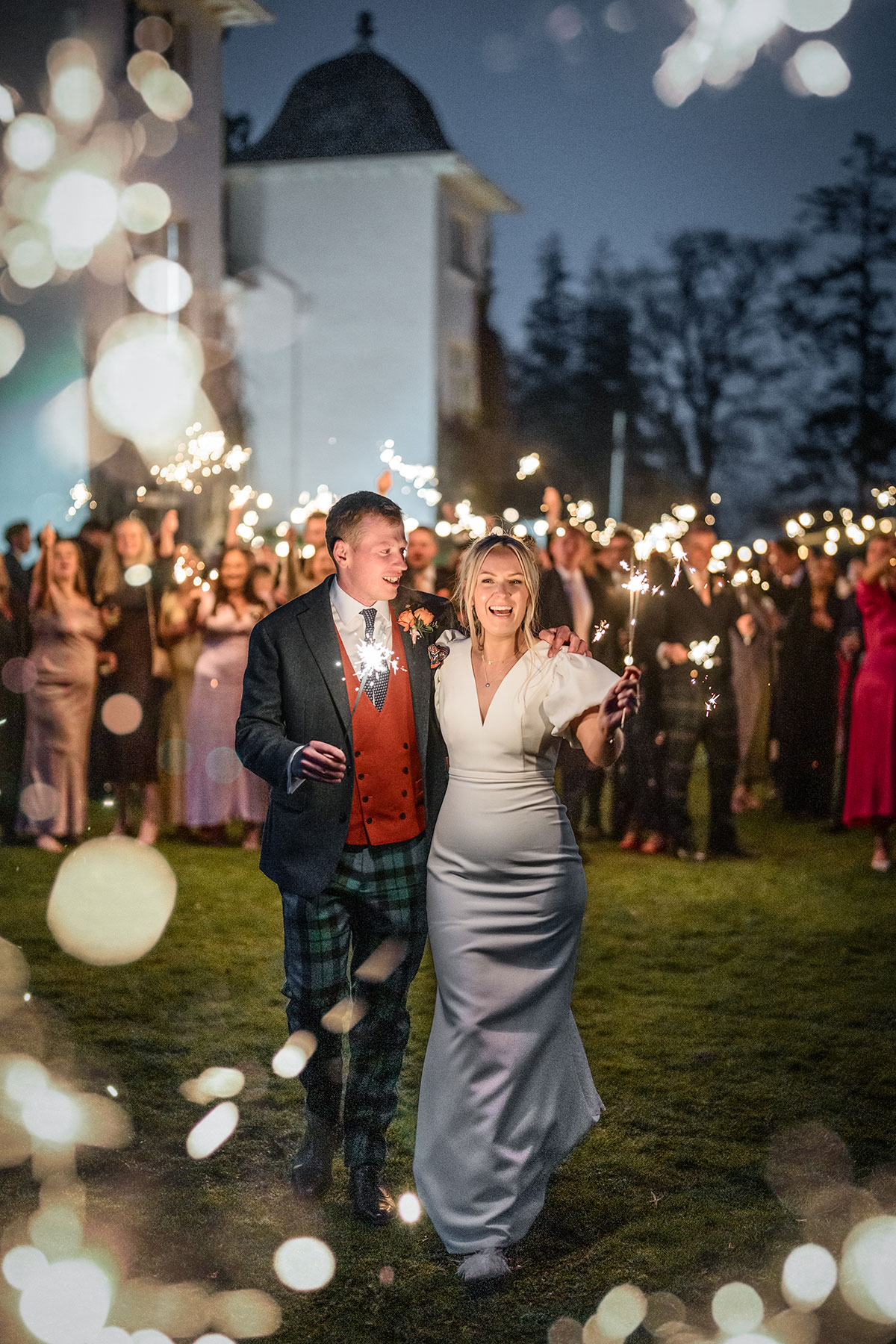 bride and groom hold sparklers with guests in the background during wedding at achnagairn castle