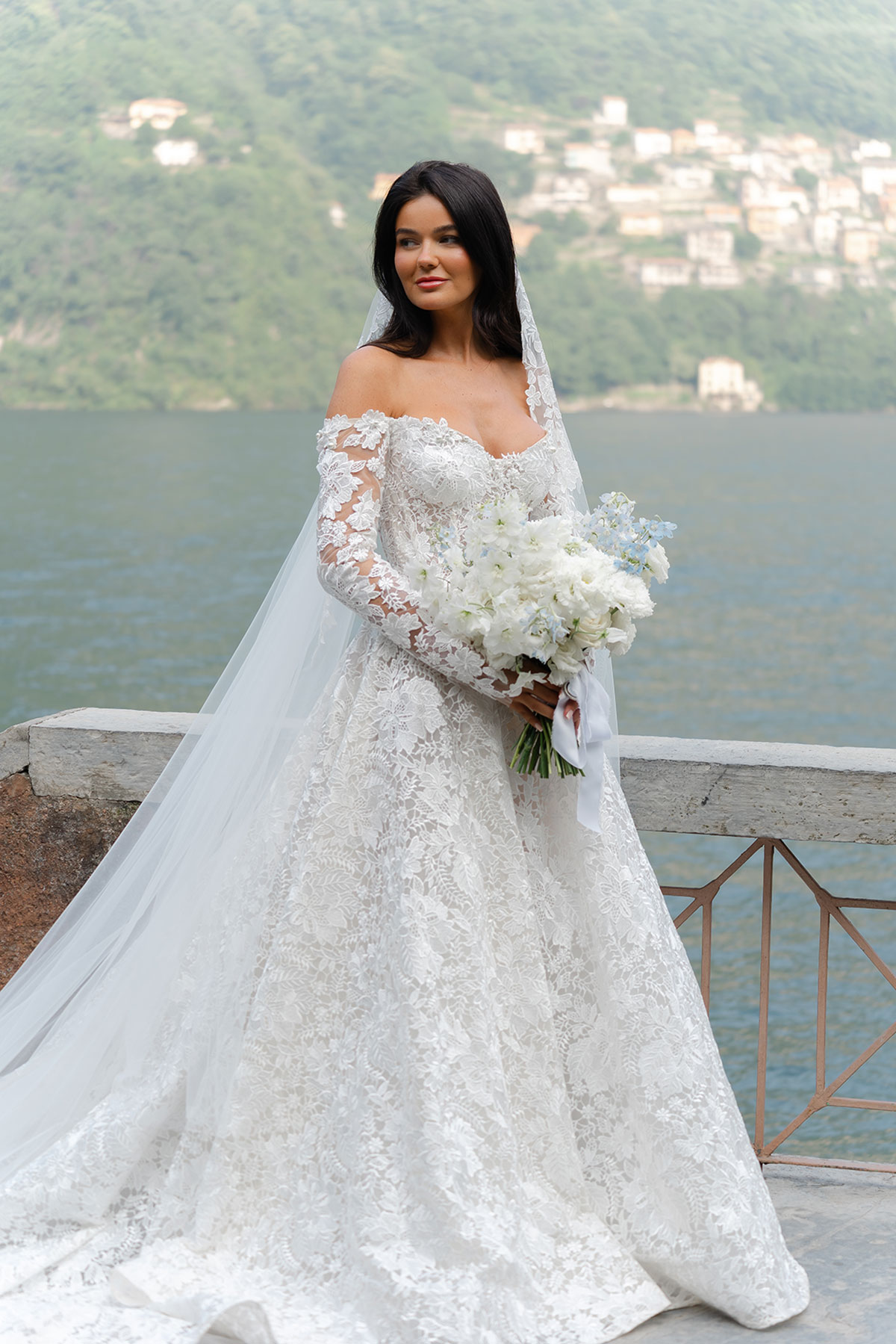 Bride holding a white and blue bouquet on the terrace at Villa Regina Teodolinda, with Lake Como in the background.