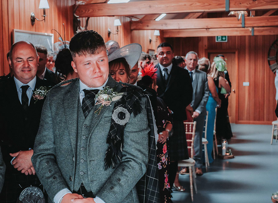 a tearful groom wearing a tartan fly plaid wells up as wedding guests wait behind him