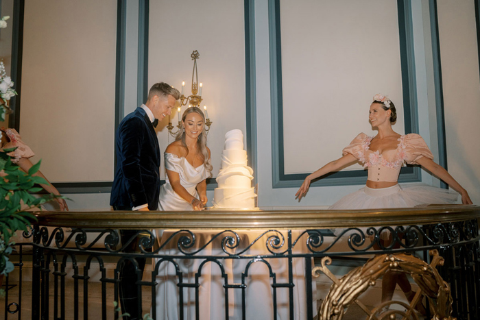 Bride and groom cut the cake with ballerina next to them