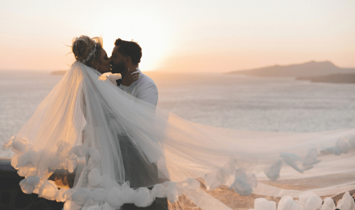 bride and groom kissing with veil flying at sunset