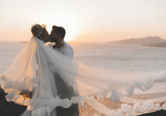 bride and groom kissing with veil flying at sunset