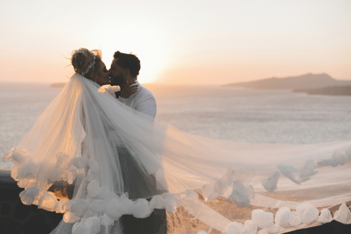 bride and groom kissing with veil flying at sunset