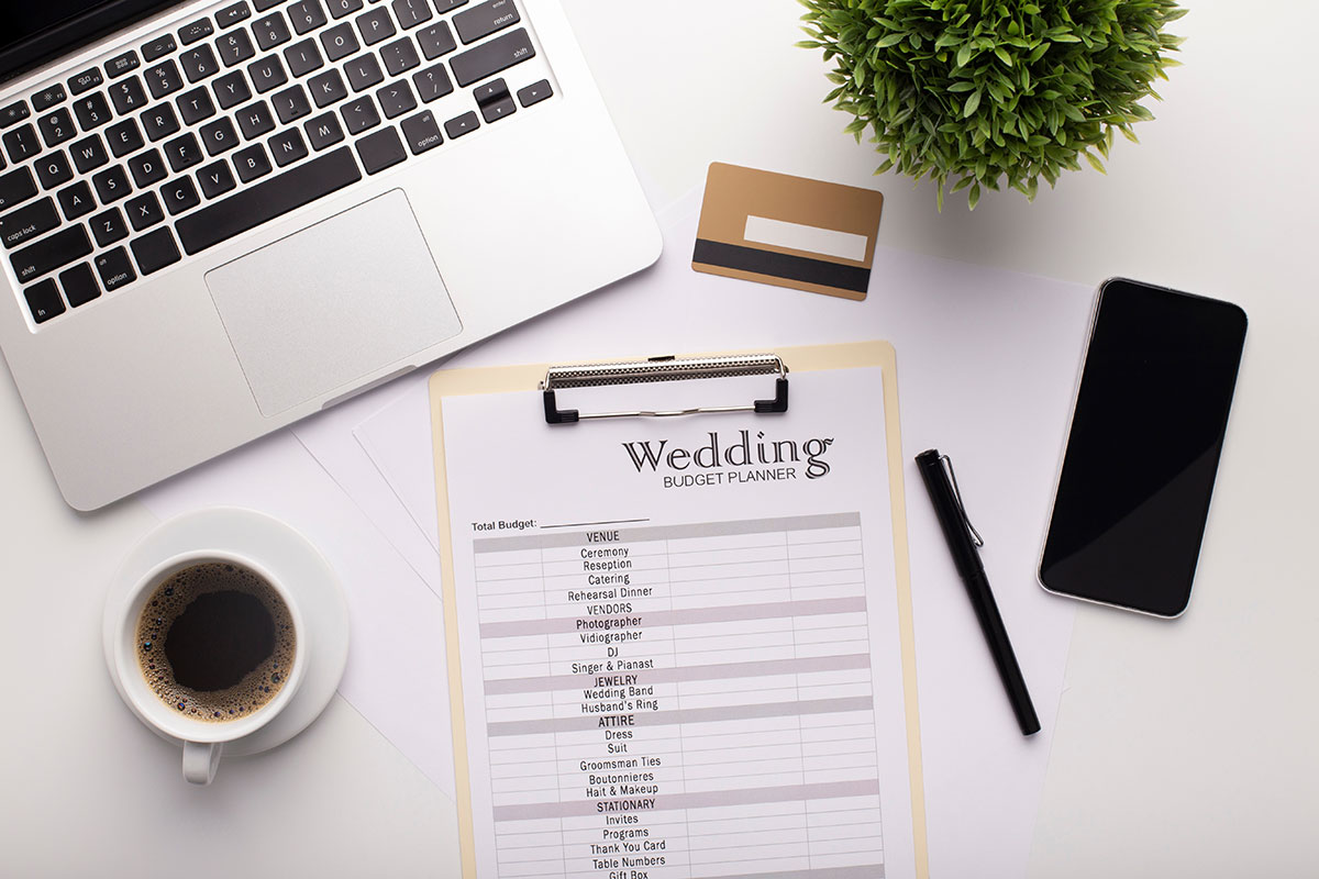stock photo of a wedding budget checklist flatlay with credit card, phone, laptop and coffee