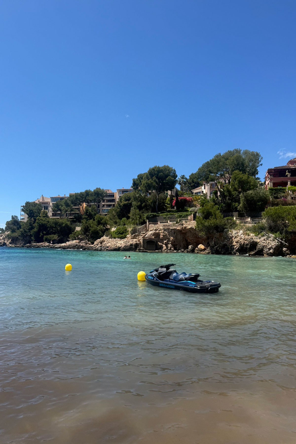 Turquoise Mediterranean bay with a jet ski anchored in crystal-clear water beneath luxury coastal villas