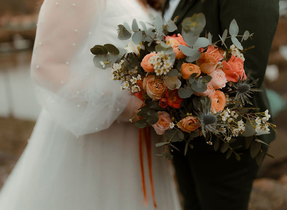 a close up of a peach pink and orange bridal bouquet shown against a wedding dress that has pearl detail