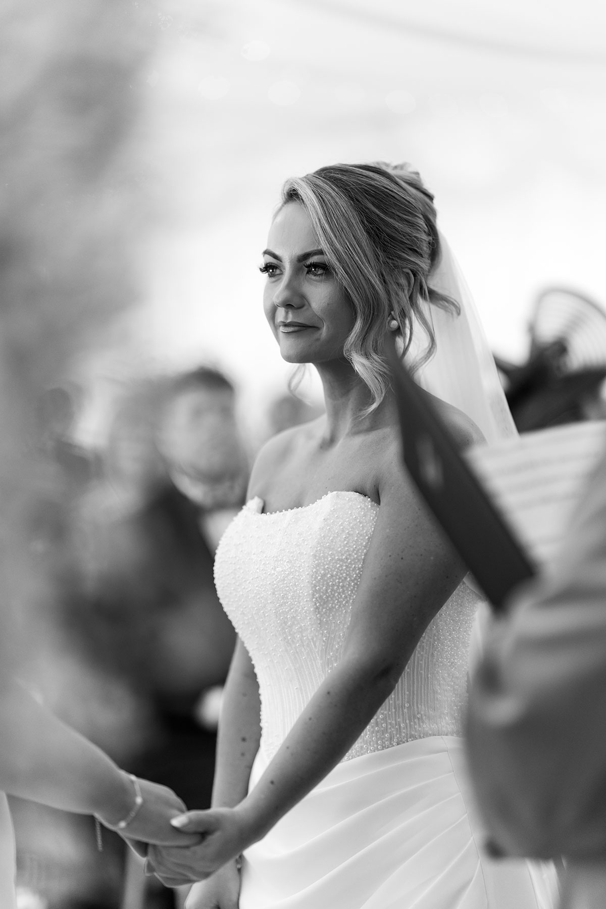 Black and white close-up of one bride during the ceremony, holding hands with her partner as they exchange vows