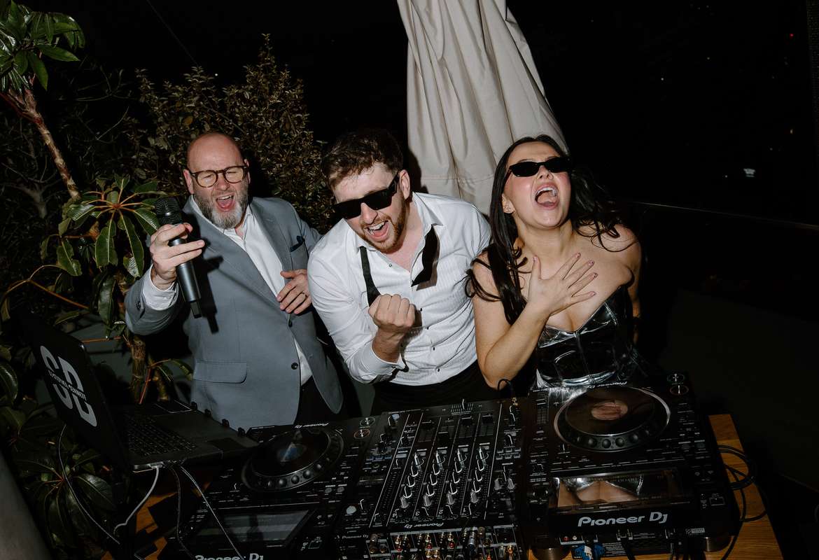 Bride and groom join the DJ behind the decks for DJ battle during their lively rooftop wedding party at The Hoxton Barcelona.