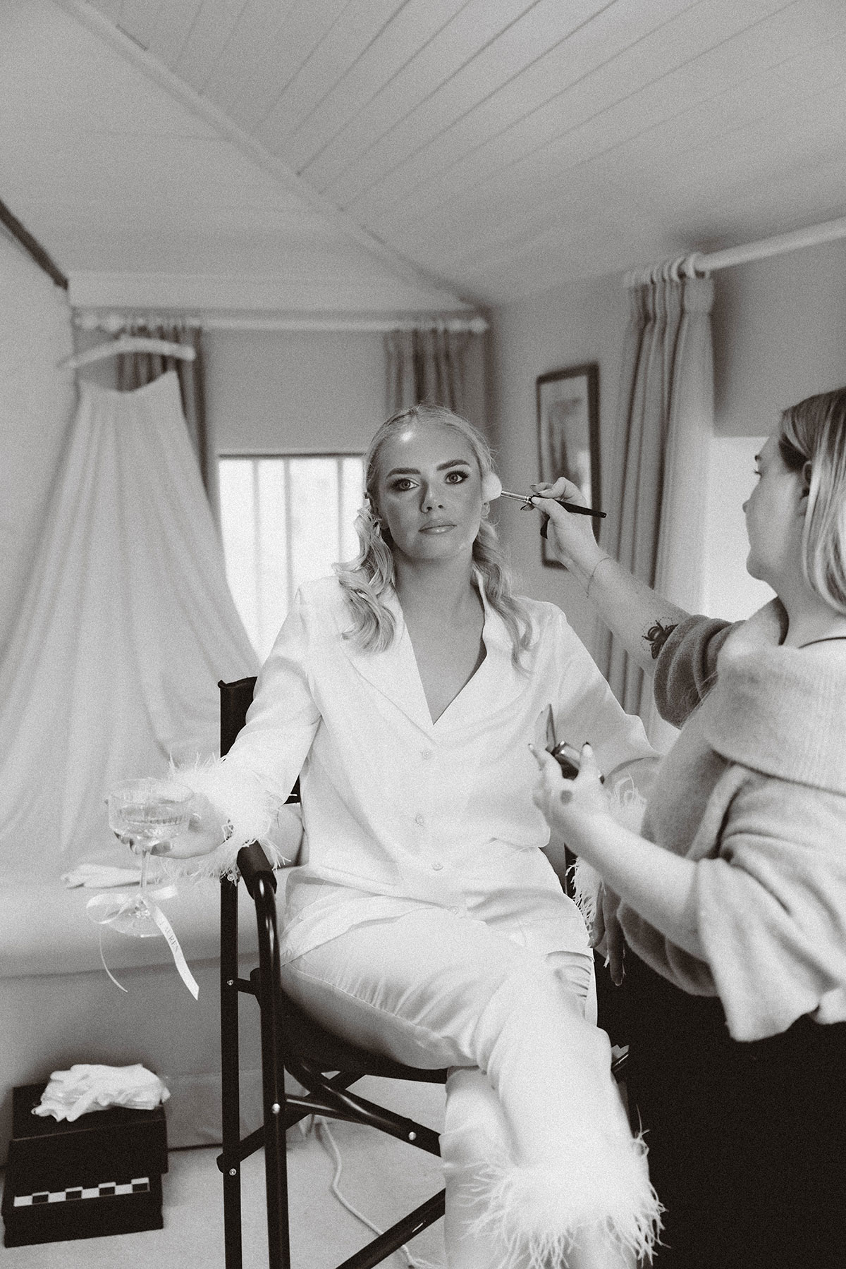 bride getting ready in feather trim pyjamas with makeup artist applying makeup in bedroom