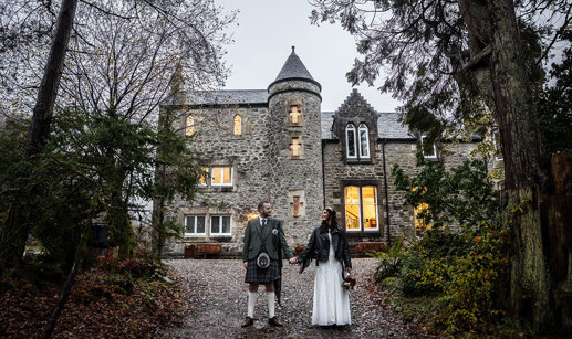 a Scottish wedding day couple holding hands outside a small castle-like building