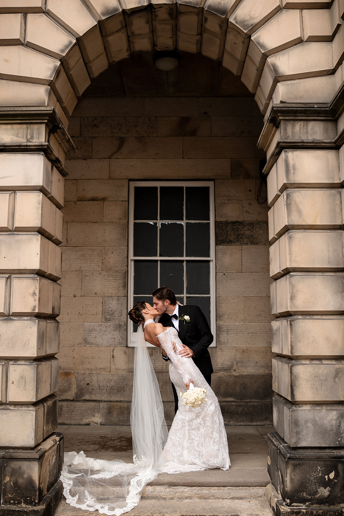 Bride and groom kiss outside The Signet Library Edinburgh under stone archway