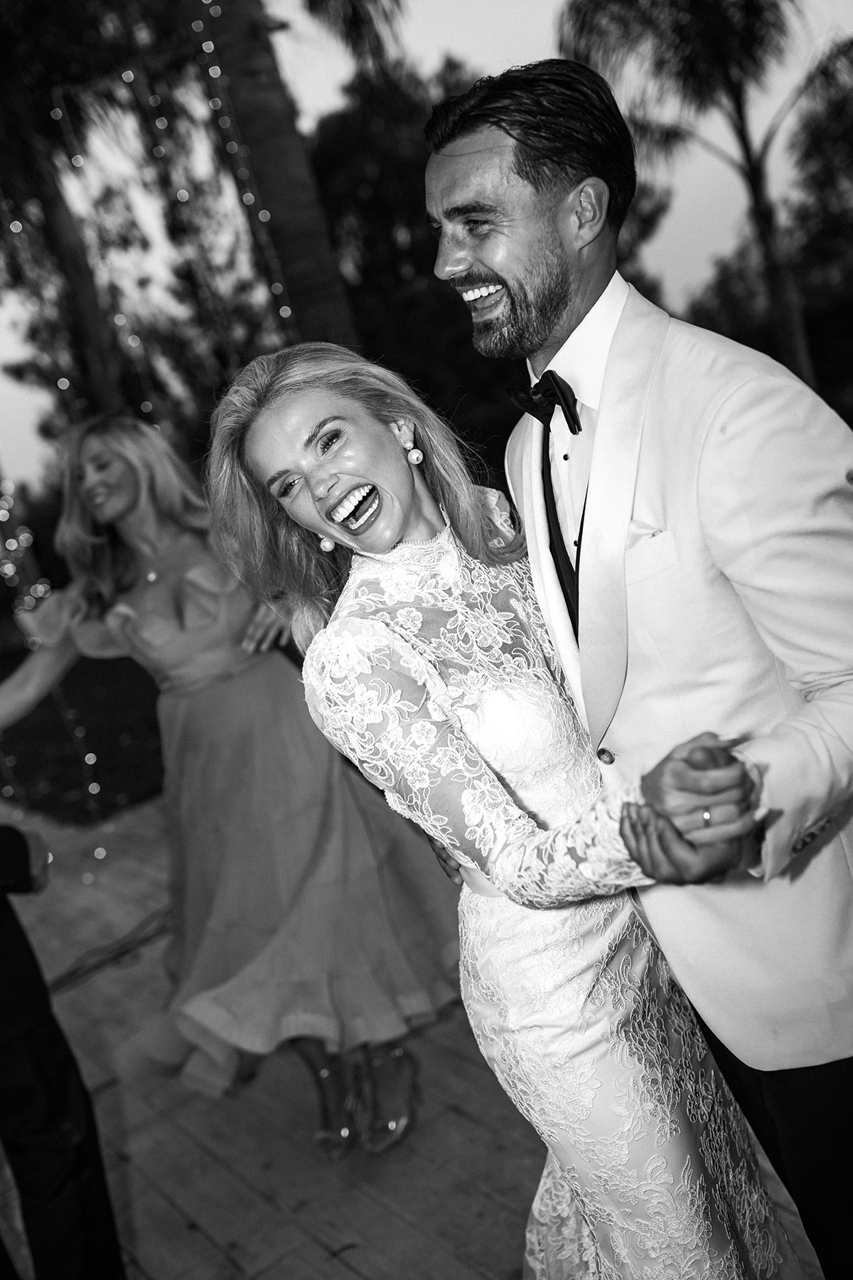 Couple share a joyful dance under twinkling lights, the bride laughing in a lace gown