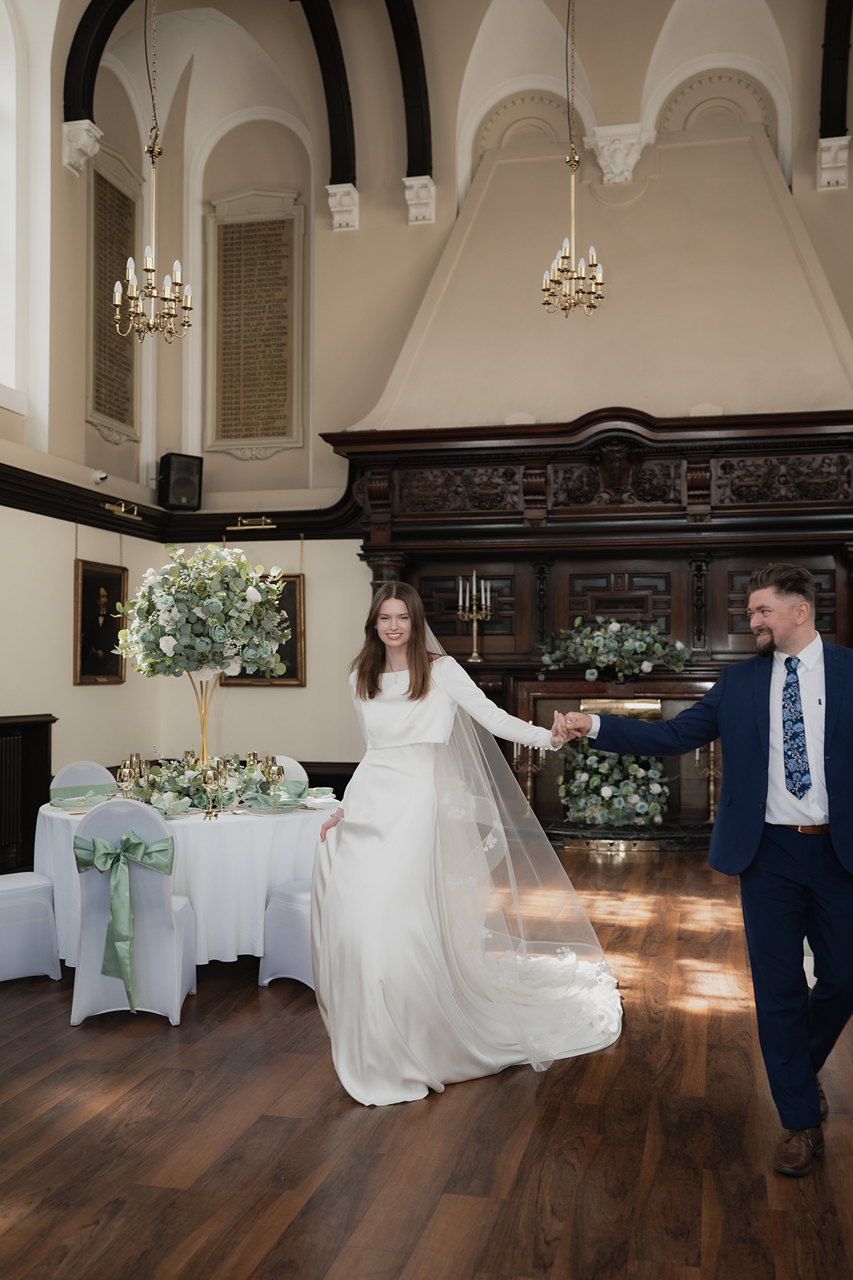 Bride and groom walking through grand reception room at 1599 at the Royal College with tall ceilings and statement floral centrepieces