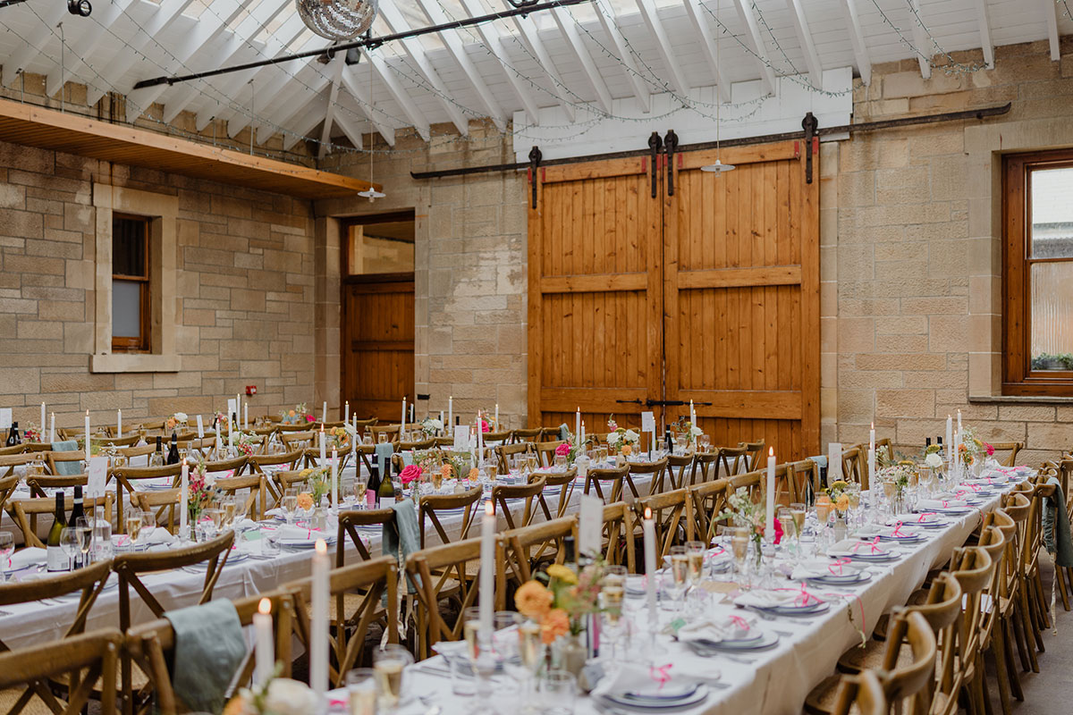 Rustic wedding reception inside Cambo Estate featuring long banquet tables, wooden chairs, candlelight and soft floral centrepieces