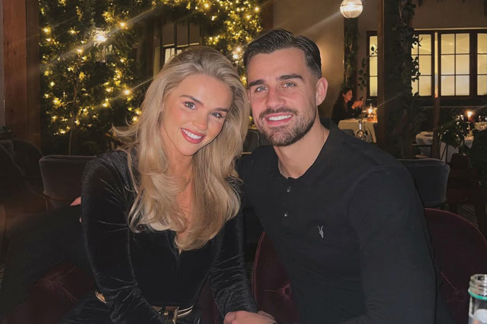 two people posing for a photo in a dark restaurant room with festive lighting behind them.