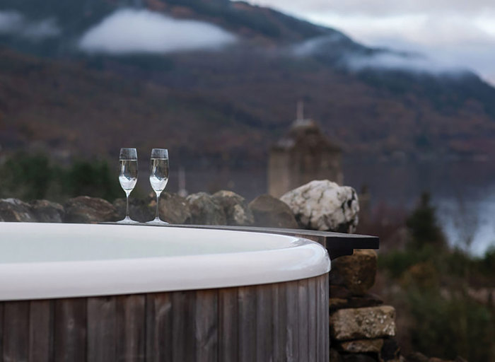 two glasses of champagne by an outdoor hot tub overlooking a mountain and lochside view