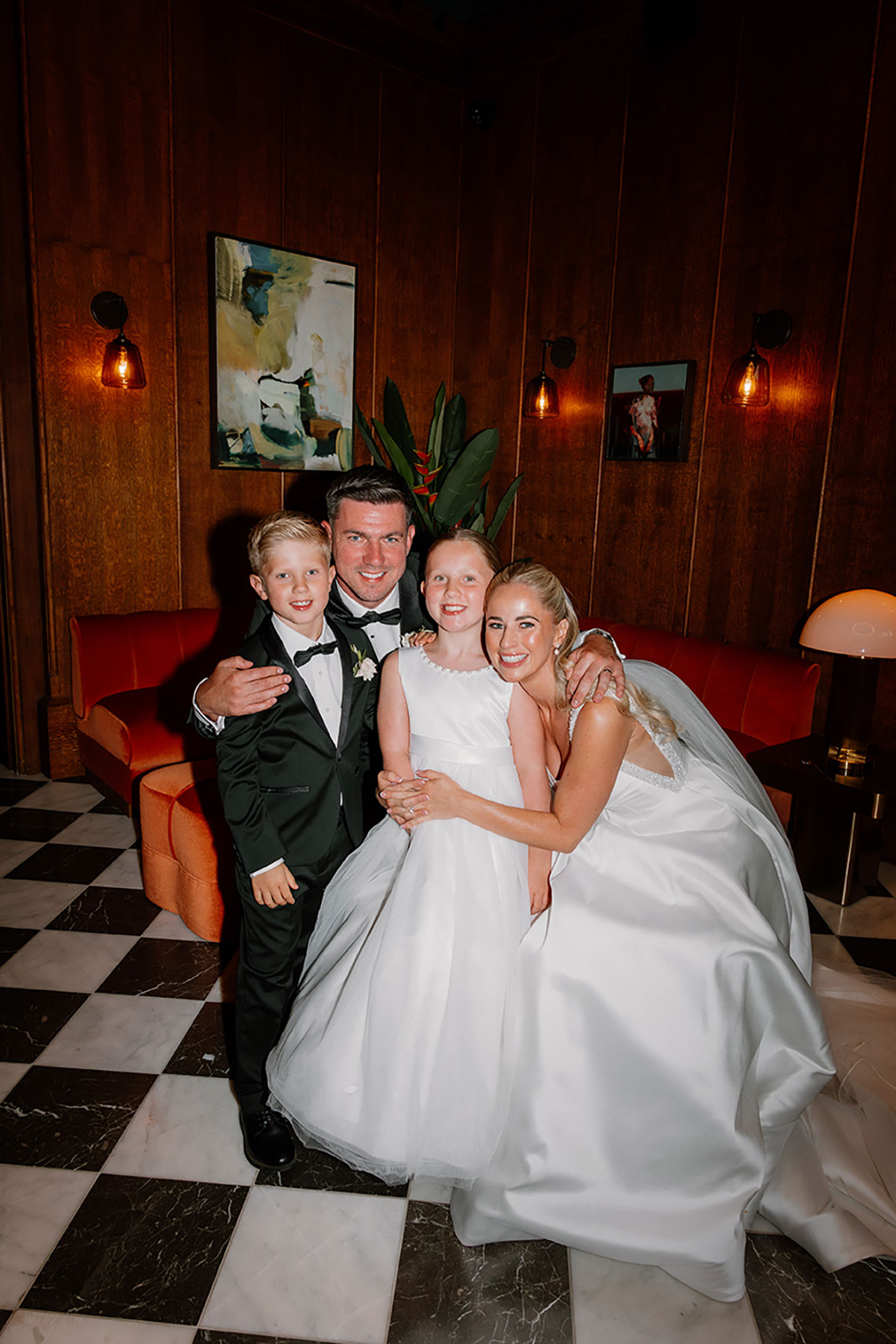 Bride, groom and two children smiling together for an evening portrait inside Mar Hall.