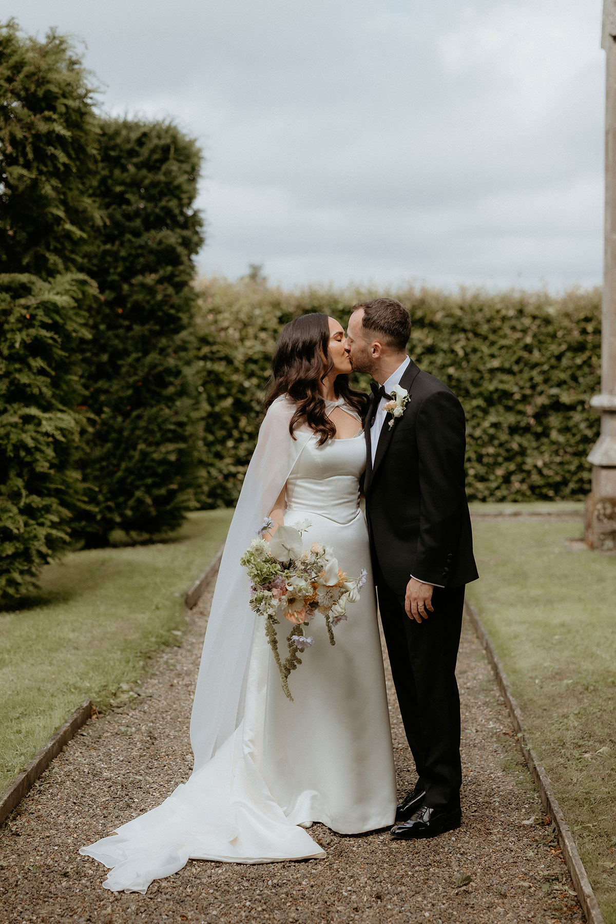 Bride and groom kissing on garden pathway at Rosebery House and Steading, Midlothian wedding venue.