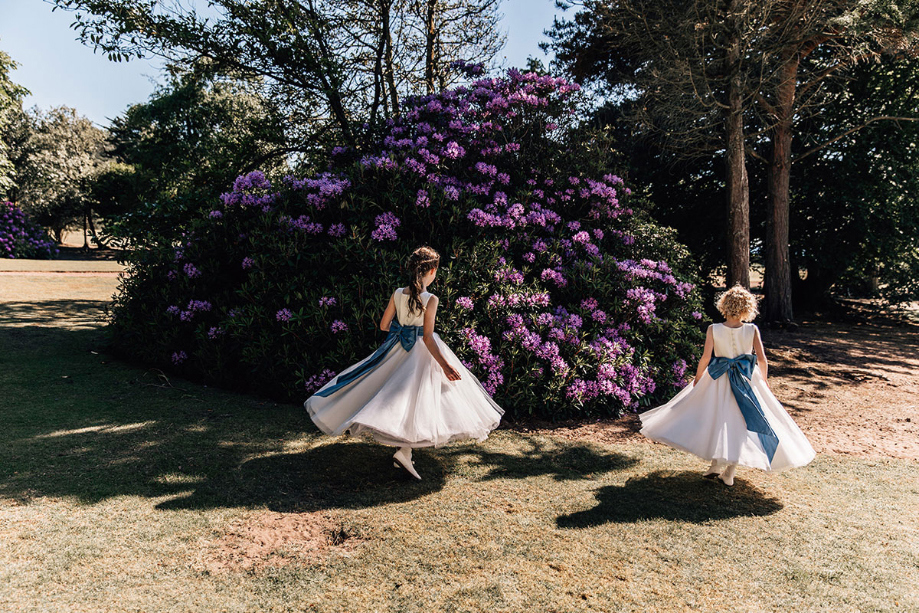 Flower girls spinning while wearing white dresses with blue bows