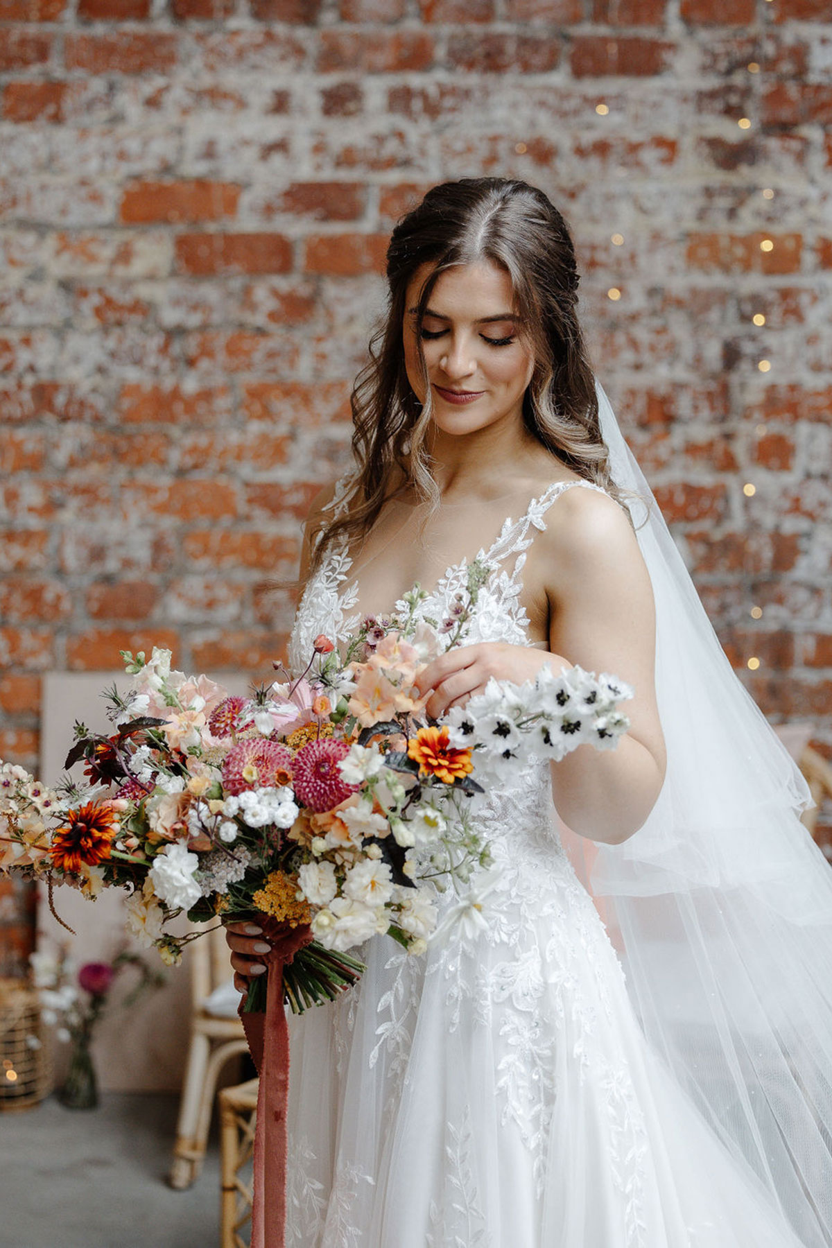 bride with strappy floral applique wedding dress and long low worn veil and holding a wildflower ribbon tied bouquet