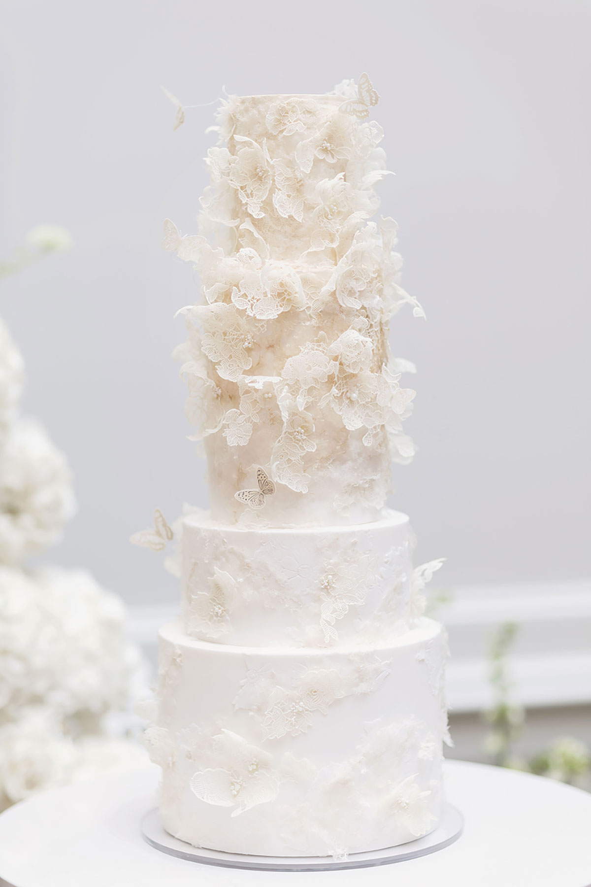 Four-tier white wedding cake decorated with lace-effect details and delicate butterfly designs