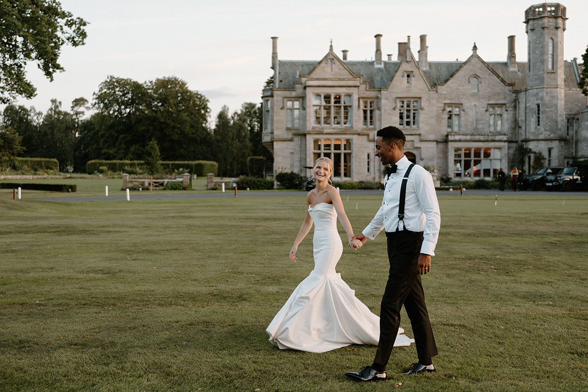 Bride and groom walking across the grounds of a historic Scottish country house wedding venue during evening portraits