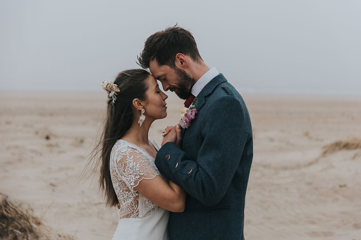 close up of bride and groom embracing on their wedding day with sand and the beach in the background
