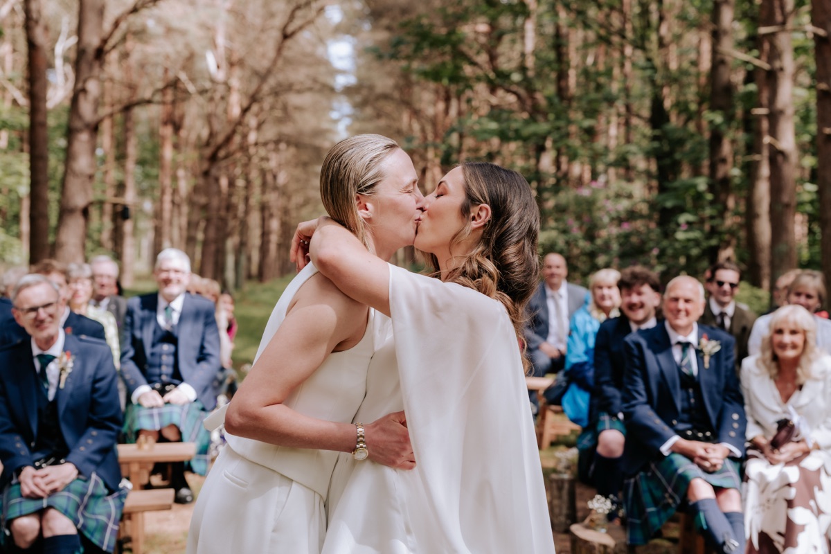 Hannah and Donna kissing during their woodland wedding ceremony at Harvest Moon.