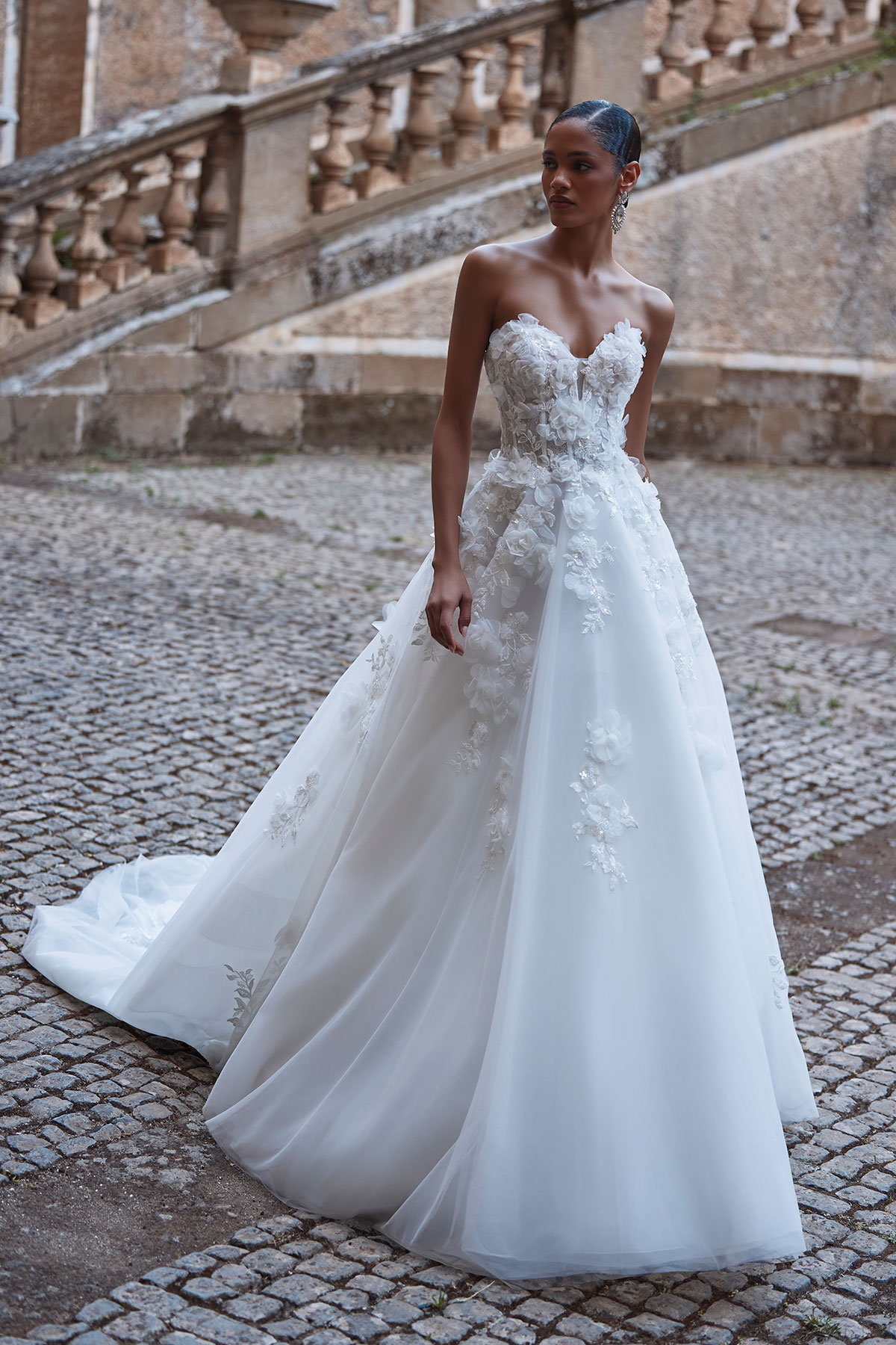 Bride wearing a sweetheart neckline wedding dress with floral appliqué bodice and soft A-line skirt, photographed outdoors on a cobbled courtyard