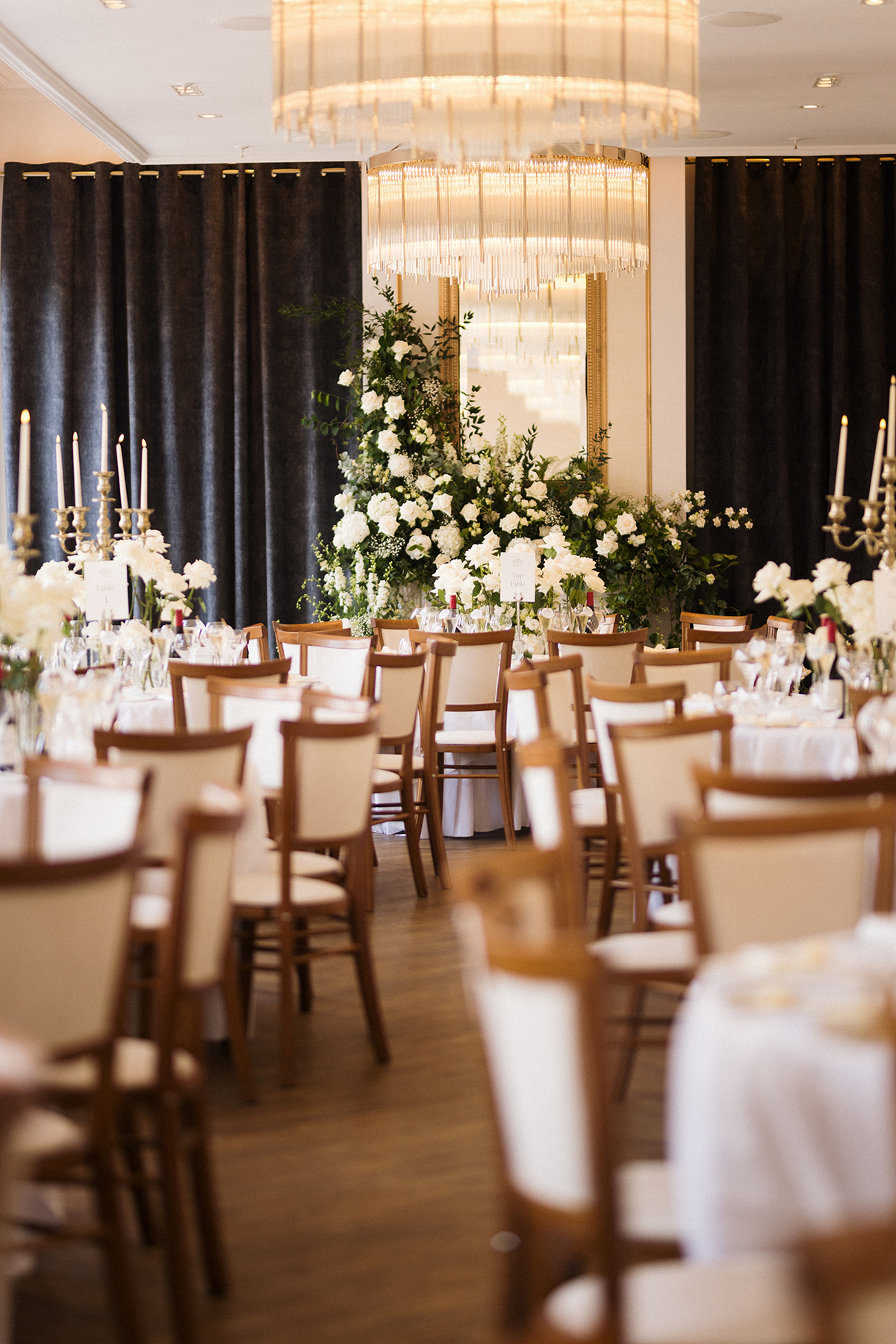 Wedding reception room styled with white flowers, candles and a floral fireplace backdrop