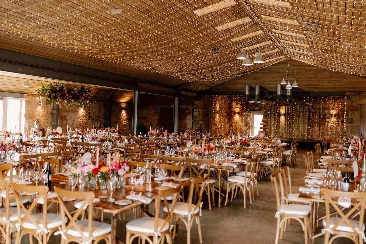 Rustic wedding reception at Falside Mill with long banquet tables, fairy lights and colourful floral centrepieces