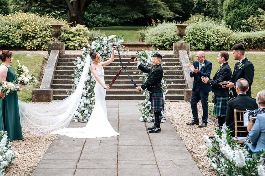 bride and groom do handfasting ritual during outdoor ceremony at mar hall