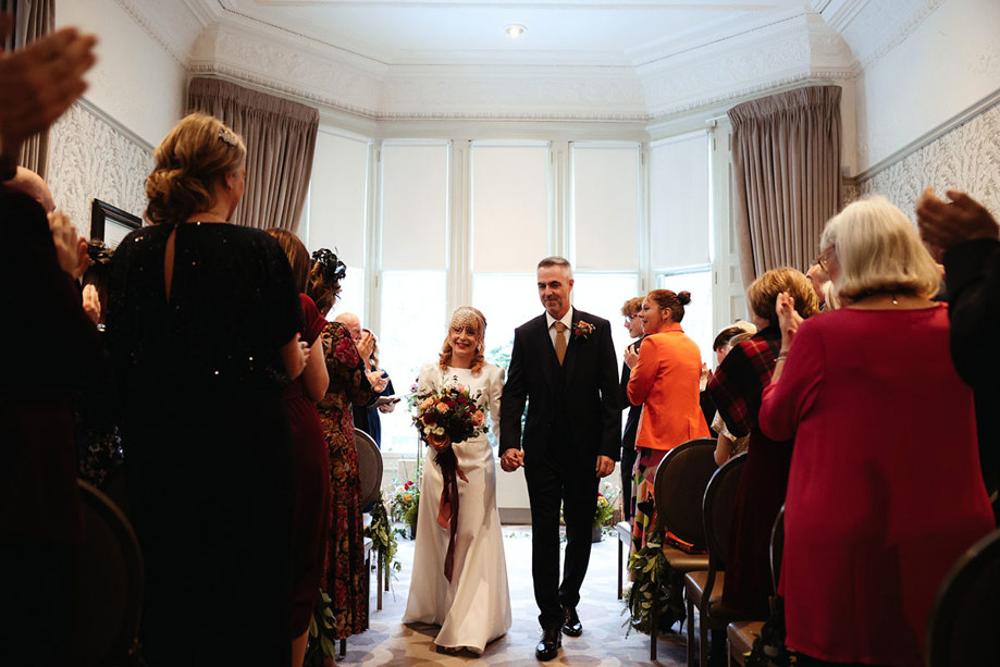 a bride and groom walk down the aisle while the guests on either side clap